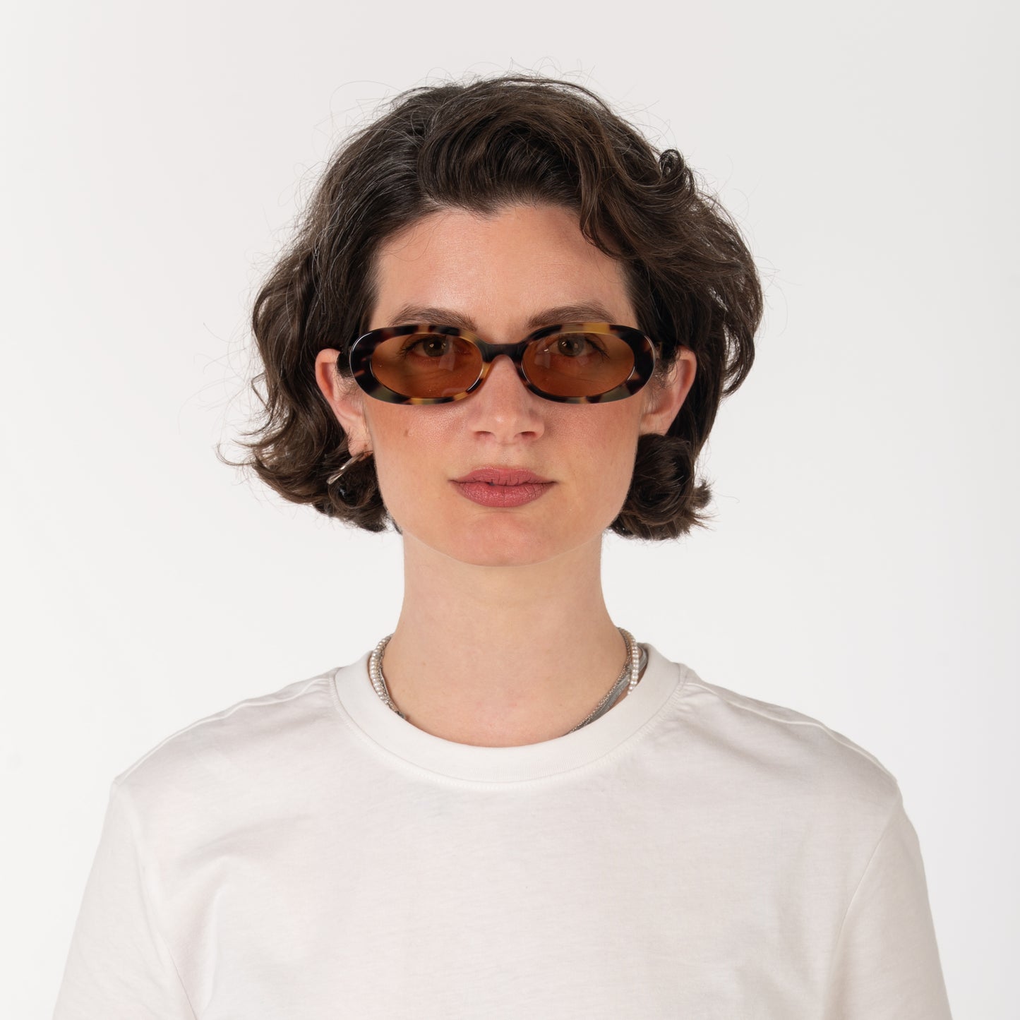 Person wearing sunglasses and a white shirt on a plain background