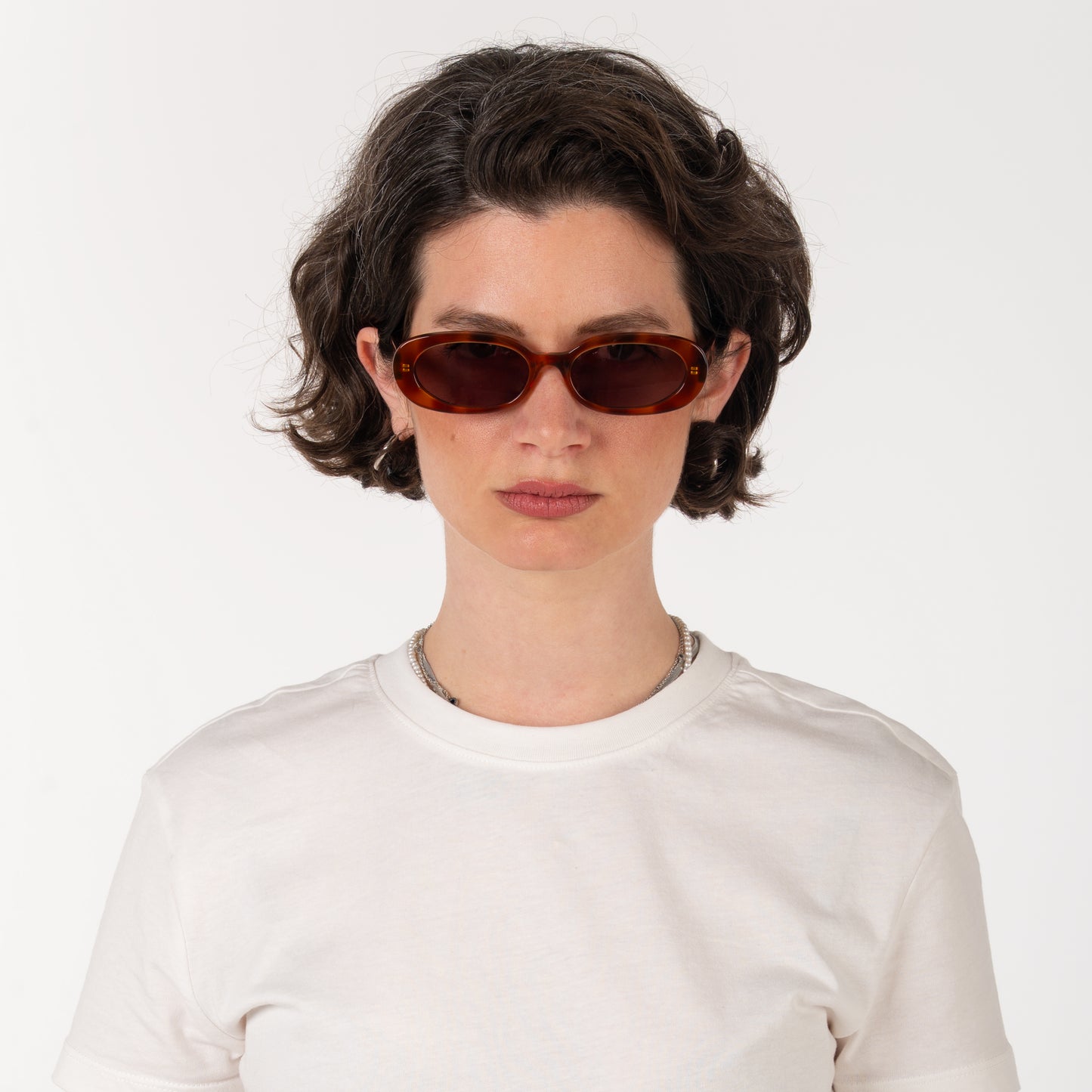 Person wearing brown sunglasses and a white shirt on a plain background