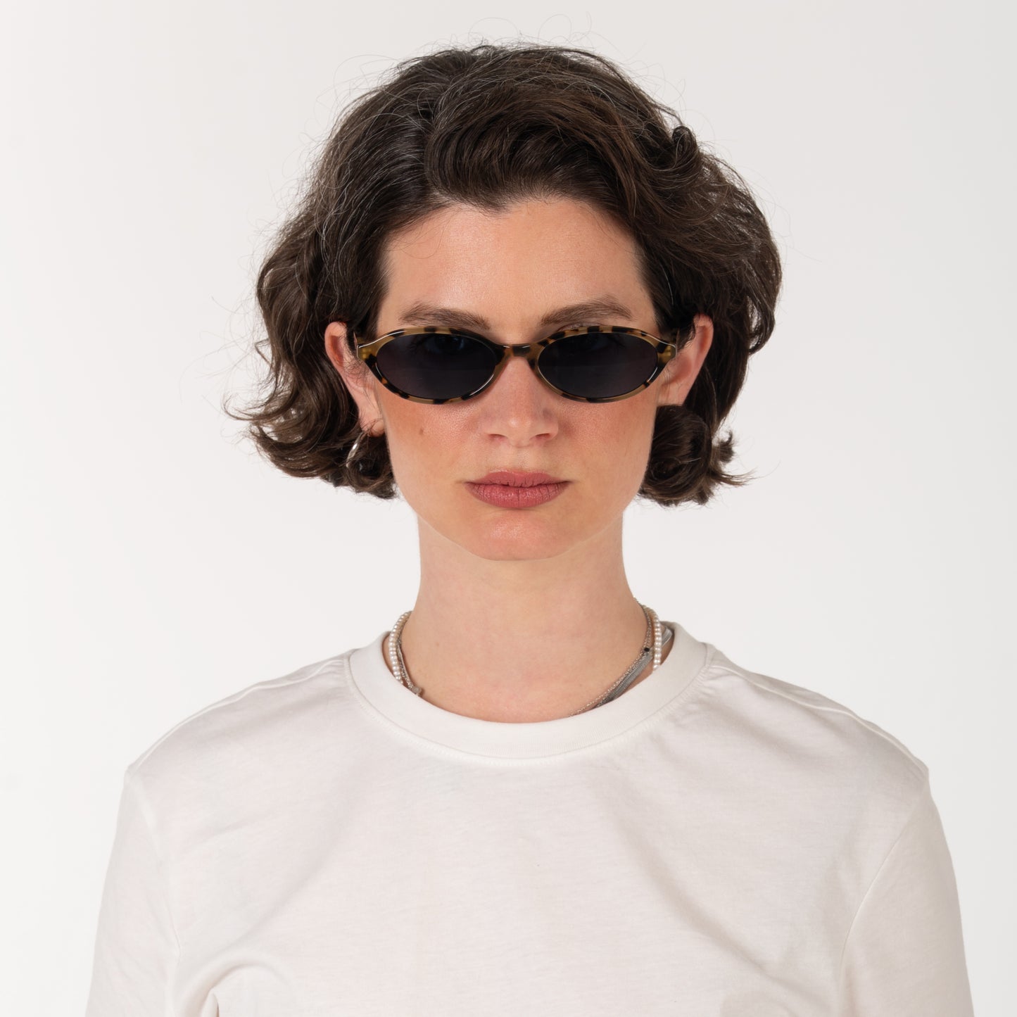 Person wearing black sunglasses and a white shirt on a light gray background