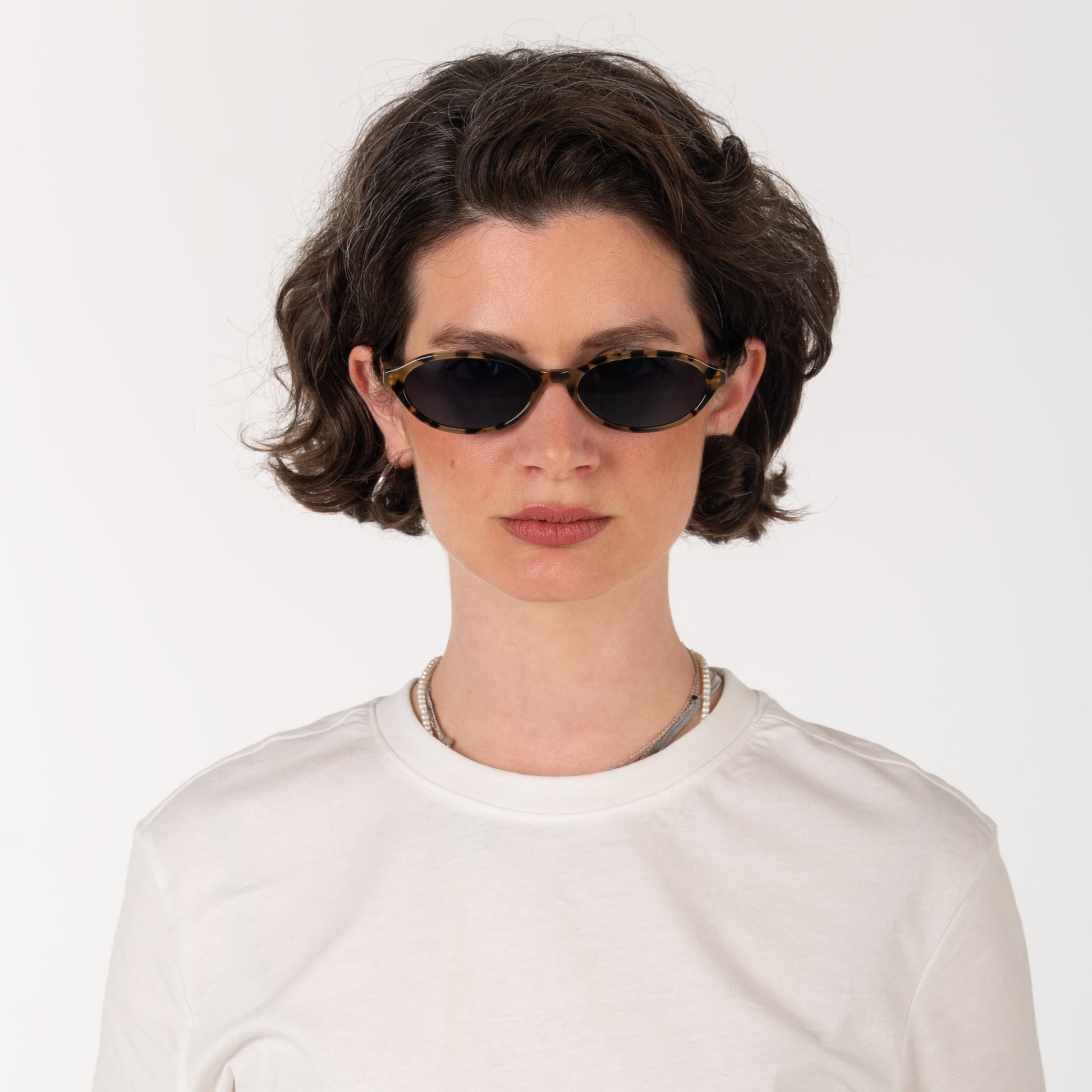 Person wearing black sunglasses and a white shirt on a light gray background