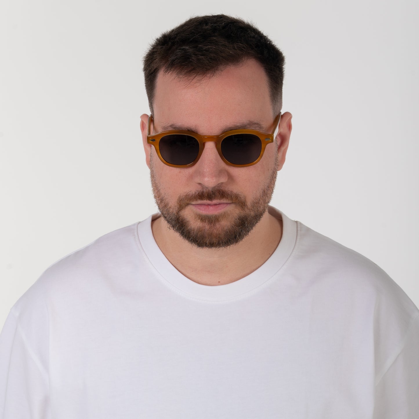 Man wearing sunglasses and a white shirt against a plain background