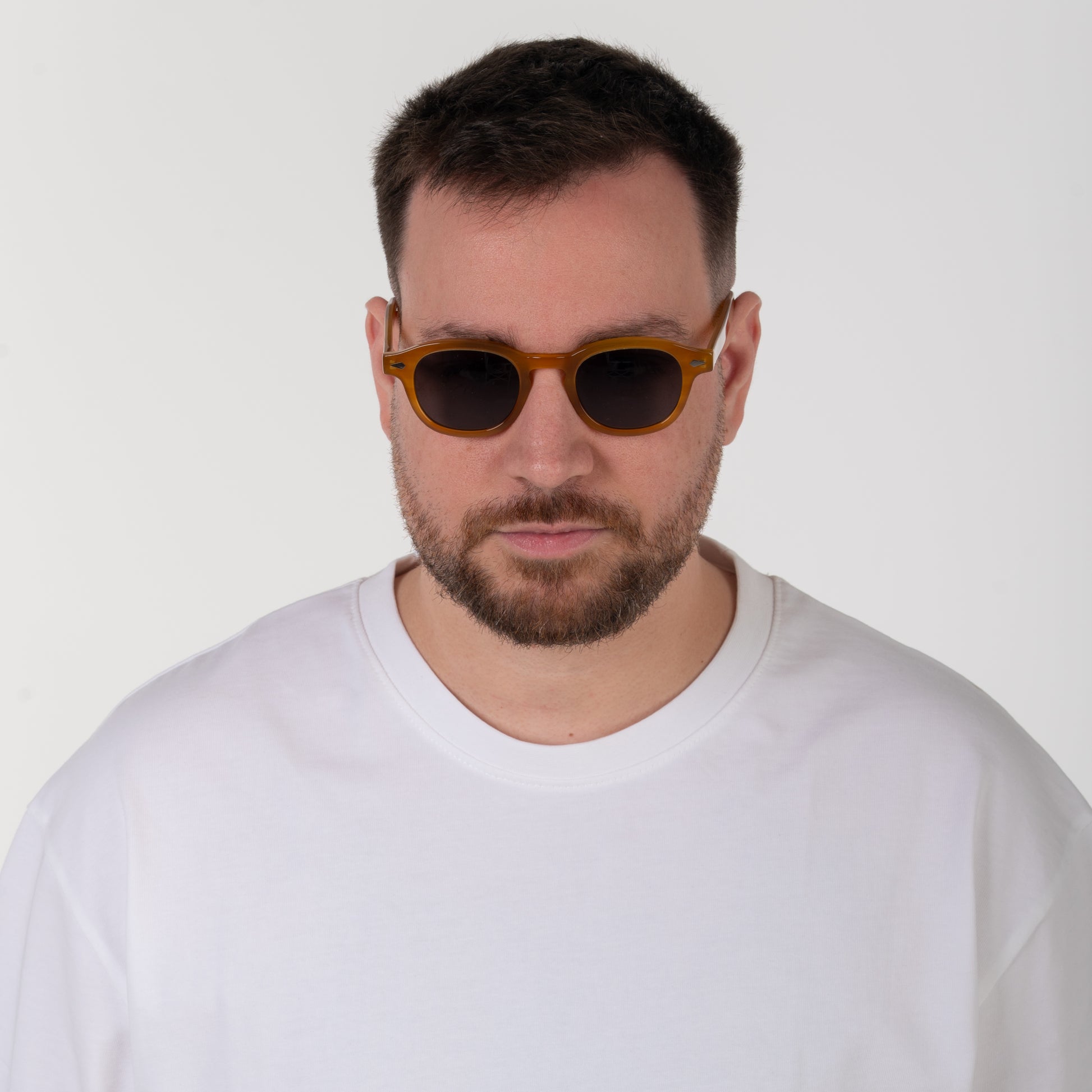 Man wearing sunglasses and a white shirt against a plain background