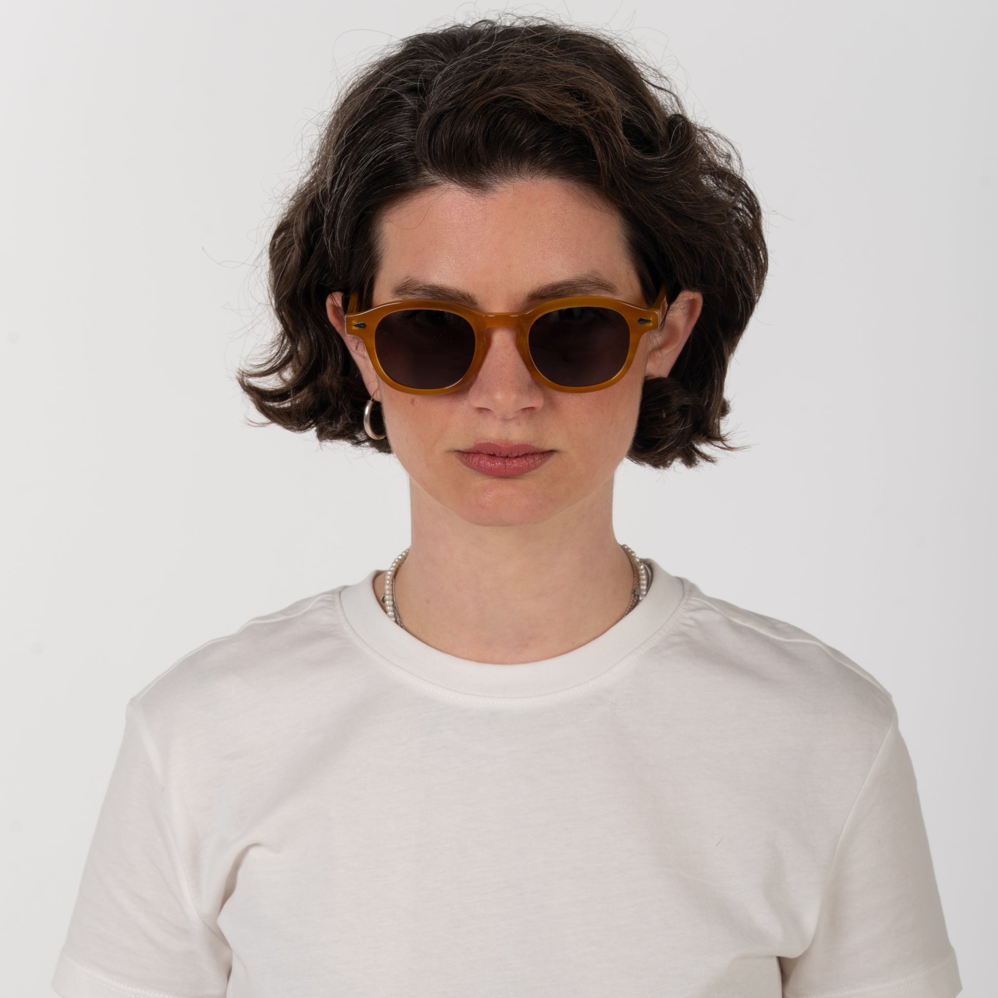 Person wearing brown sunglasses and a white shirt against a plain background
