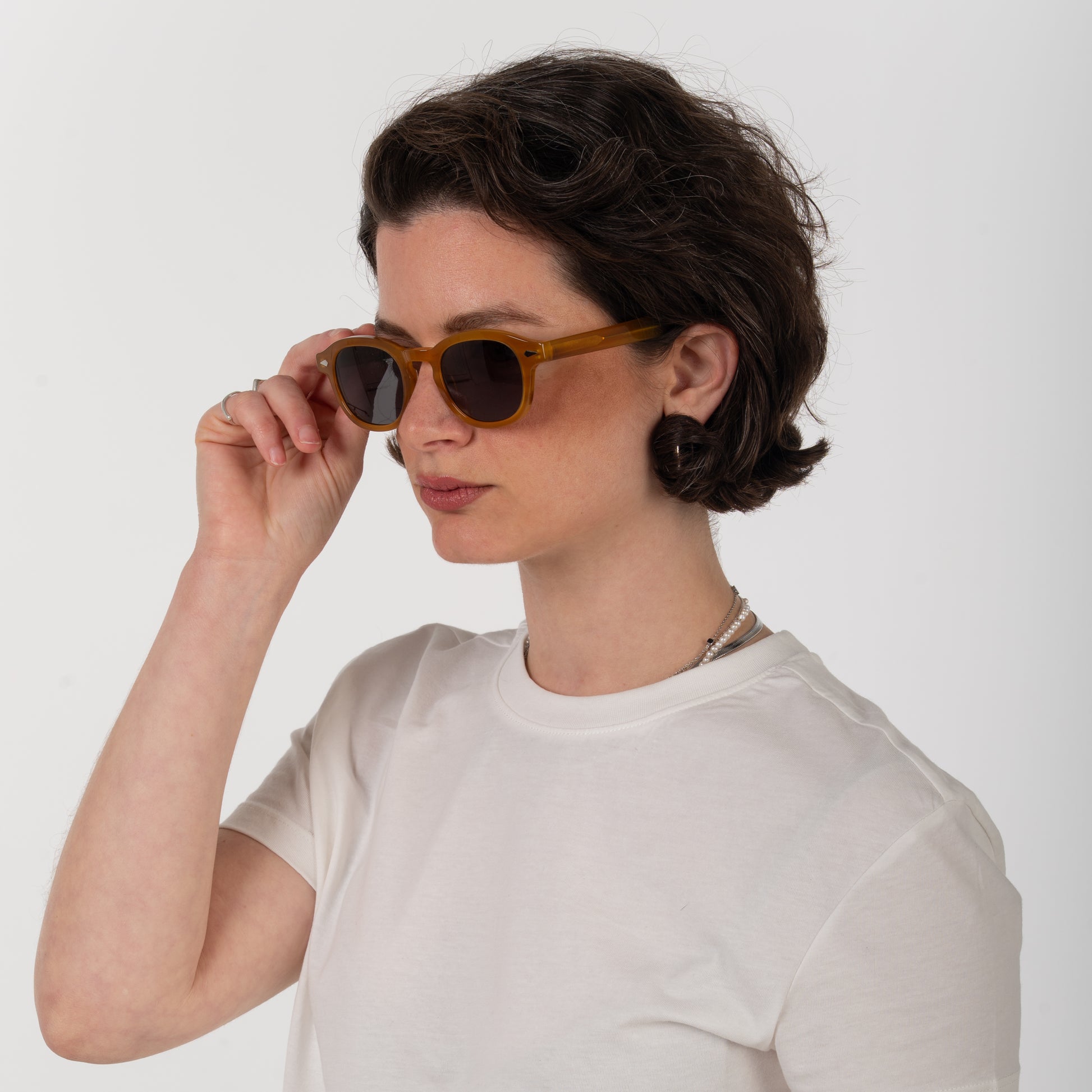 Woman wearing brown sunglasses and a white shirt against a plain background