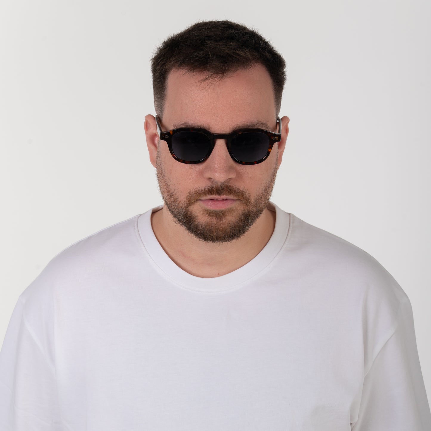 Man wearing black sunglasses and a white shirt against a plain background