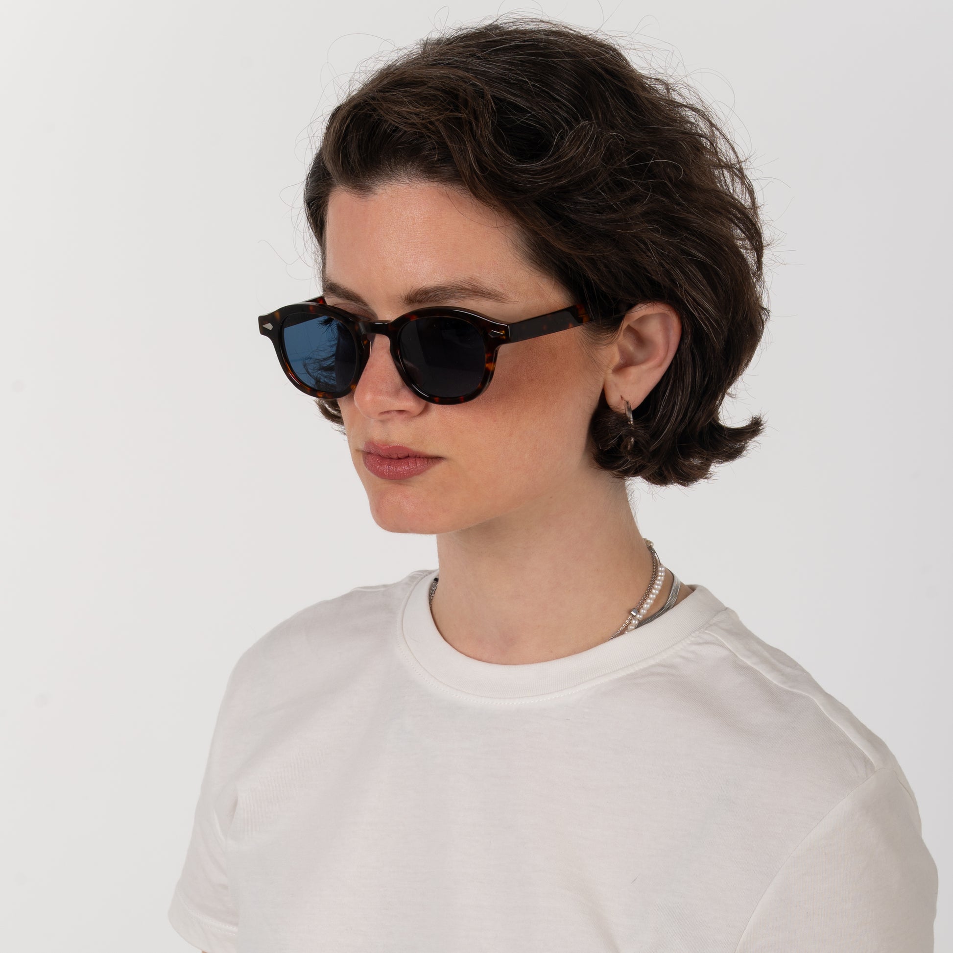Person wearing black sunglasses and a white shirt on a plain background