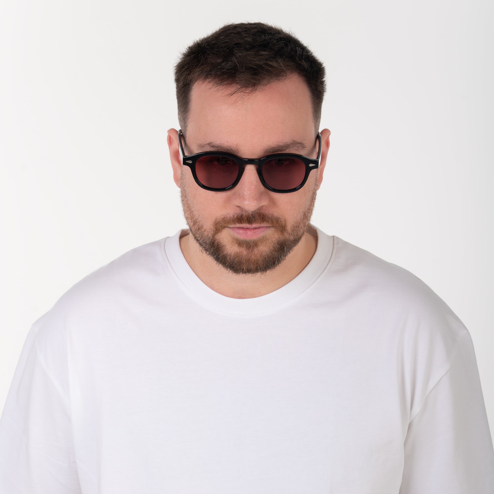 Man wearing dark sunglasses and a white shirt against a plain background