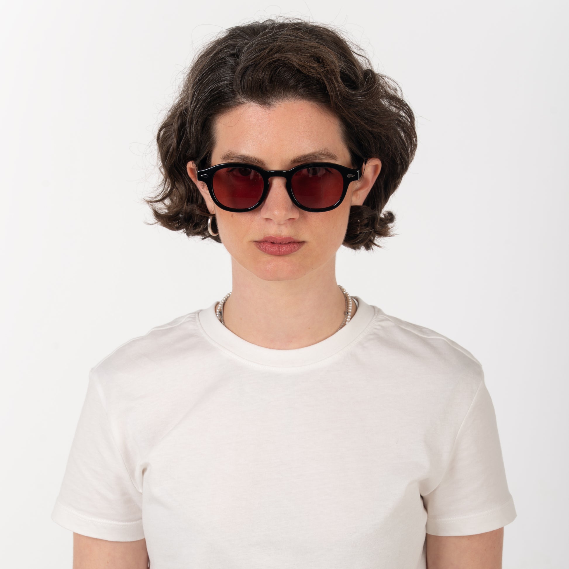 Person wearing red sunglasses and a white t-shirt on a plain background